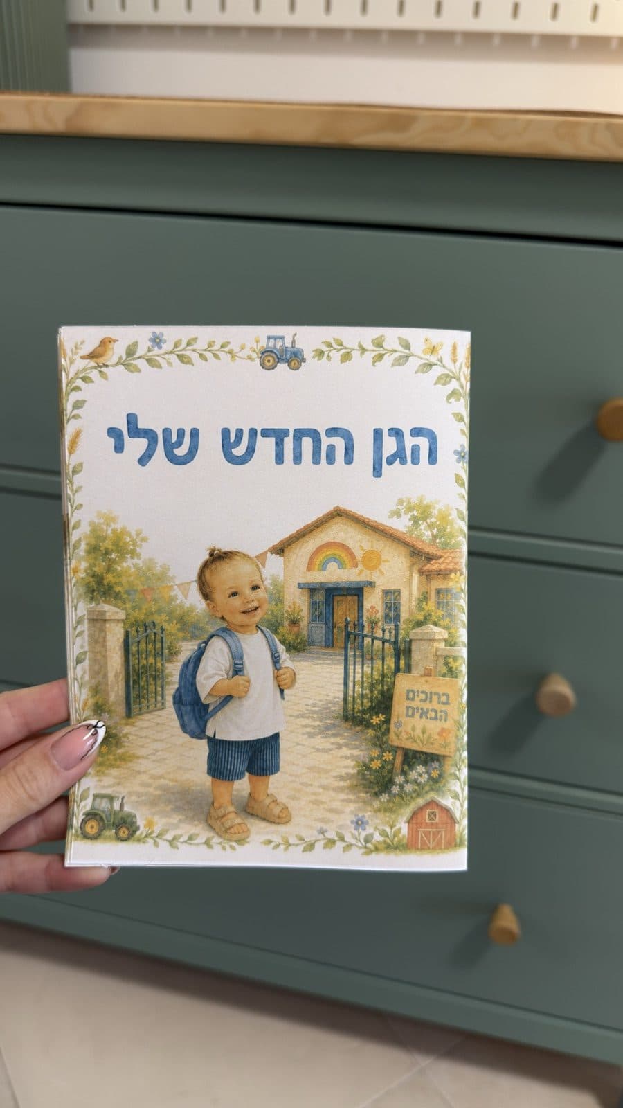ספר אישי ׳הגן החדש שלי׳ ביד, עם איור של ילד עם תיק גב מול הגן