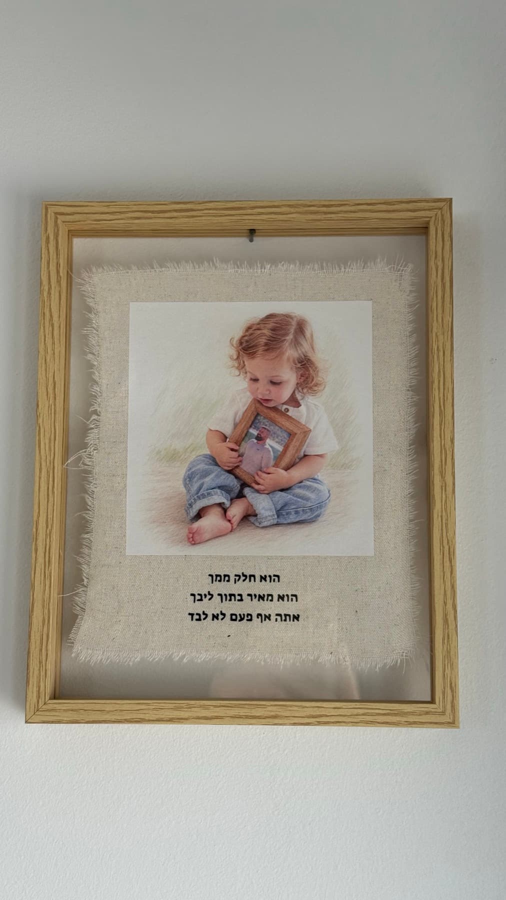 תמונת בד ממוסגרת: ילד יושב ומחזיק מסגרת תמונה קטנה, עם טקסט אישי מתחת על בד פשתן